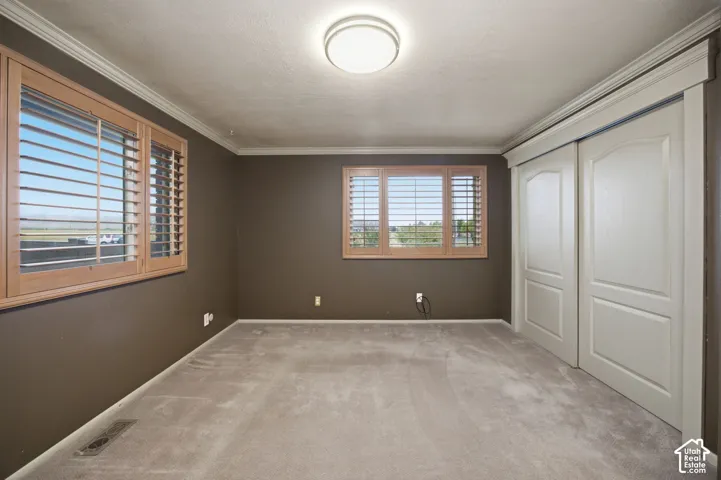 Primary Bedroom featuring carpeted flooring, crown molding, double-panel sliding closet doors, and windows fitted with plantation shutters