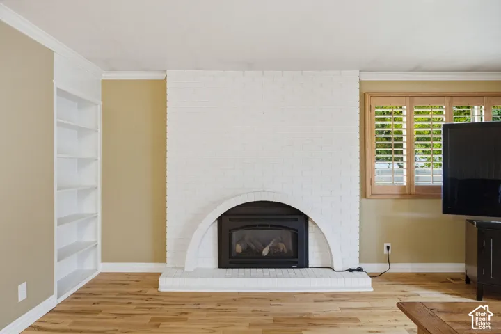 White painted brick fireplace featuring an arched surround, wood-finish flooring, built-in recessed shelving, and louvered wood shutters