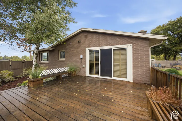 Expansive wood-finish deck featuring built-in bench seating, brick exterior, sliding glass door, and wooden perimeter fencing