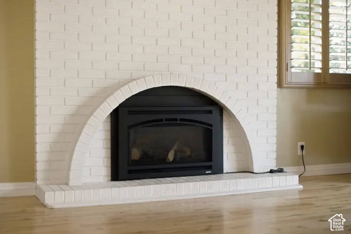 Fireplace featuring a white-painted brick surround, arched masonry detail, black metal firebox insert, and wood-finish flooring