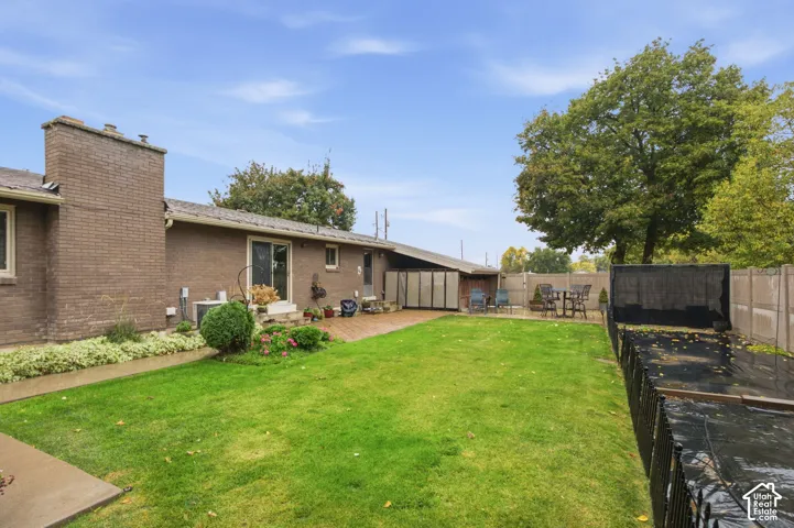 Backyard featuring a brick exterior wall, masonry chimney, brick-paved patio, manicured lawn, and perimeter fencing