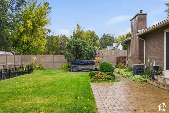 Fenced backyard featuring a brick exterior, paver patio, integrated brick chimney, and manicured lawn