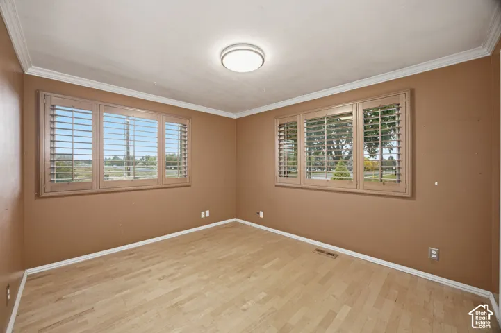 Bedroom #2 featuring light wood-finish flooring, crown molding, and two windows equipped with interior plantation shutters