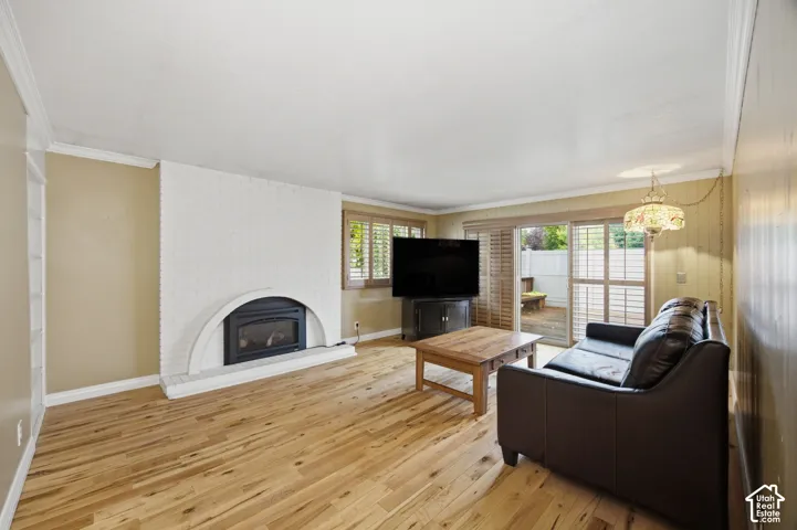 Living area featuring wood-finish flooring, white brick fireplace with an arched surround, wood-slat window shutters, and sliding glass doors