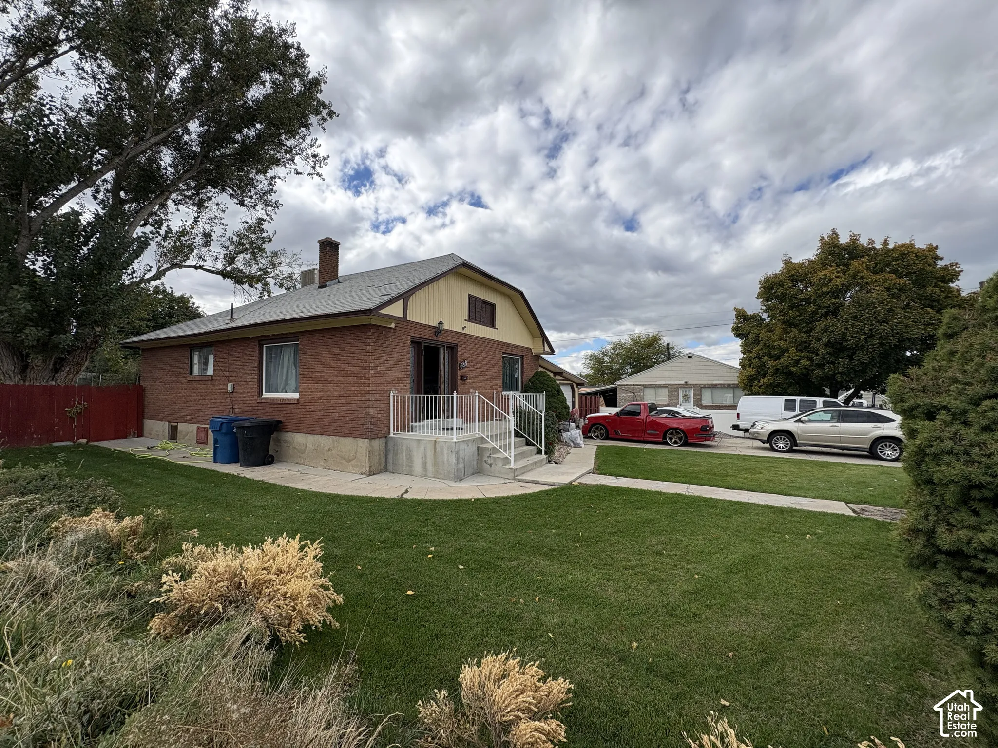 Single-story brick exterior featuring a shingled roof, concrete porch with metal railing, and expansive lawn area