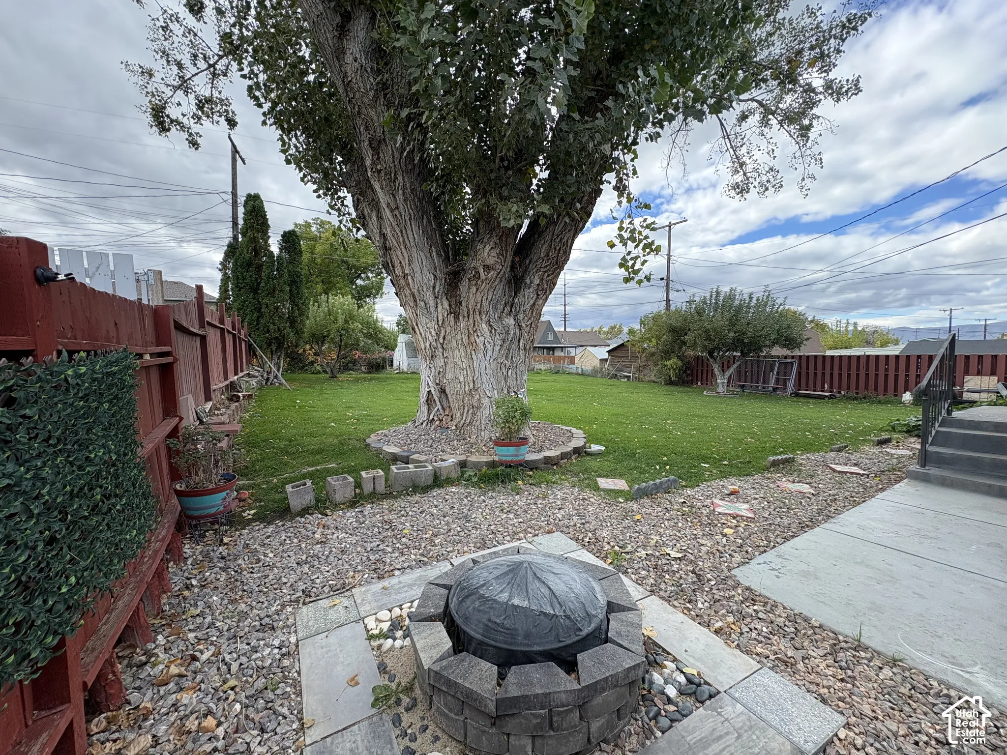 Backyard featuring a stone-encased fire pit, expansive lawn, mature tree, stone-tile patio area, and privacy fencing