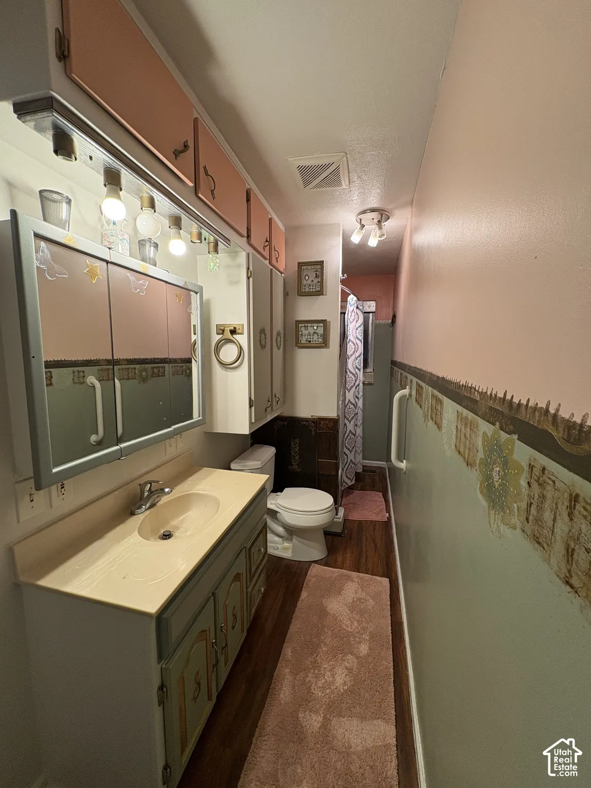 Bathroom featuring wood-finish flooring, vanity with integrated basin, mirrored medicine cabinet, and built-in upper cabinetry