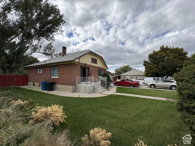 Single-story brick exterior featuring a shingled roof, concrete porch with metal railing, and expansive lawn area