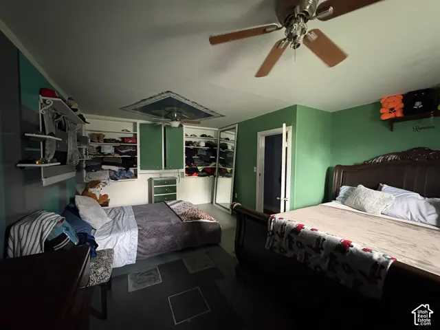 Room featuring integrated wall shelving, ceiling-mounted paddle fan, and a mirrored closet door