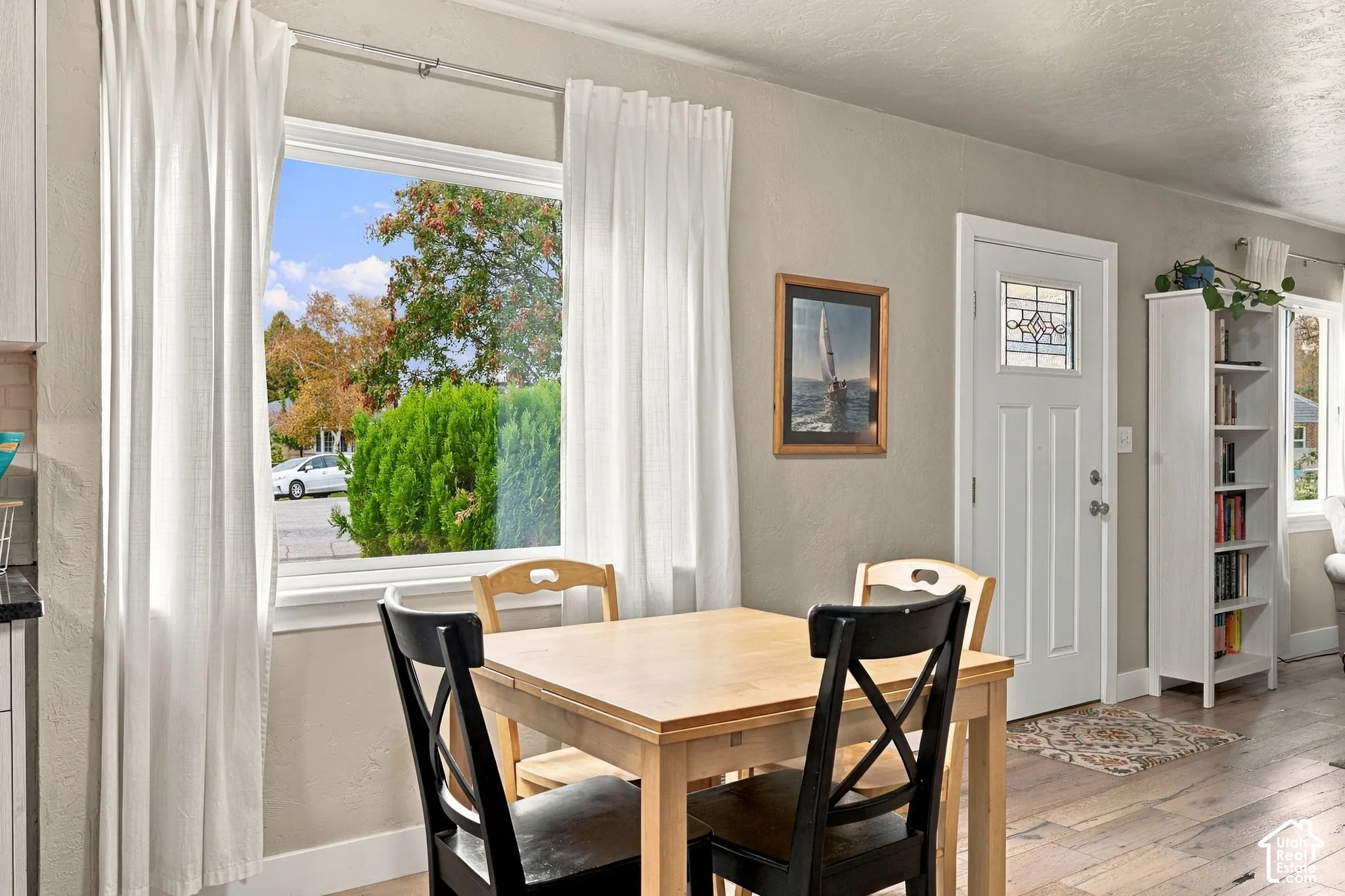 Large picture window, white exterior door with decorative glass inlay, and wood-finish flooring