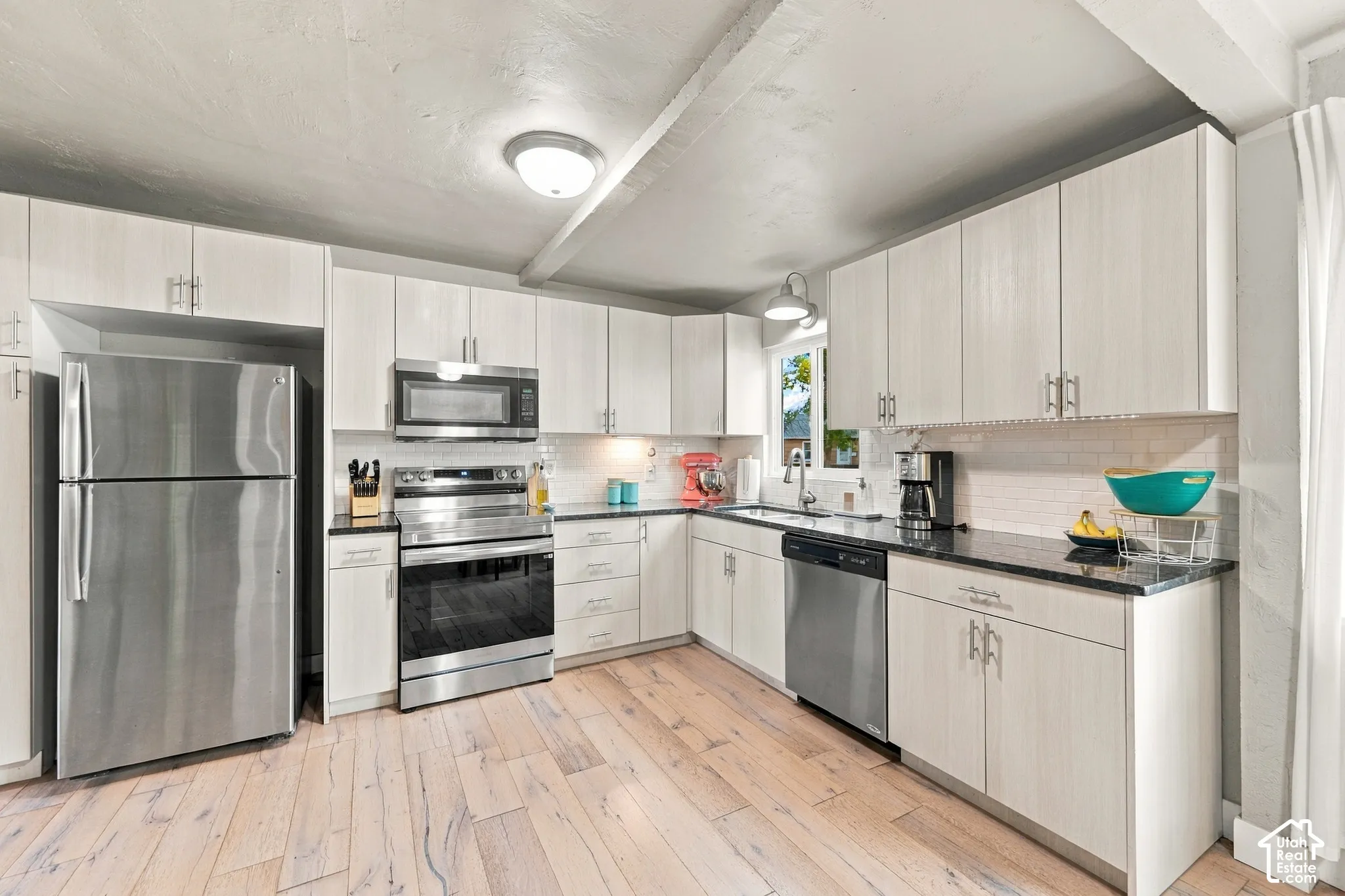 Kitchen featuring light-toned cabinetry, stainless steel appliances, subway tile backsplash, and wood-finish flooring