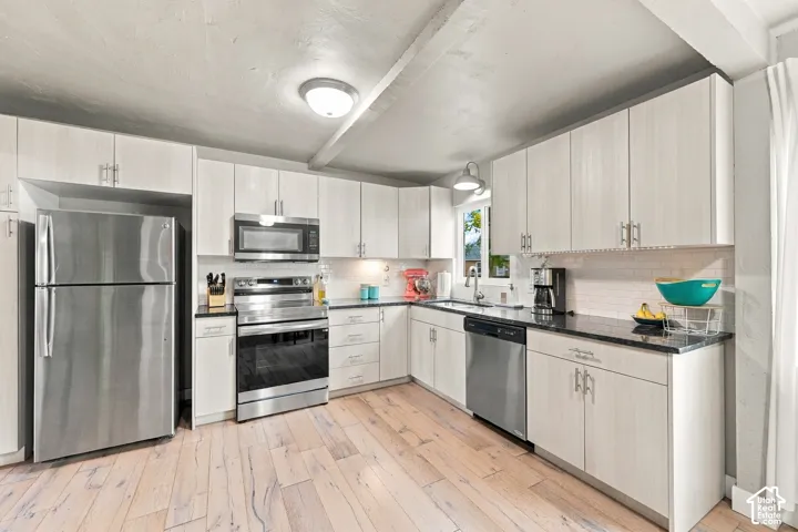 Kitchen featuring light-toned cabinetry, stainless steel appliances, subway tile backsplash, and wood-finish flooring