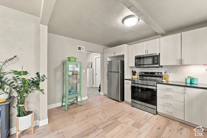 Kitchen featuring light-finish cabinetry, wood-finish flooring, stainless steel appliances, and a tiled backsplash