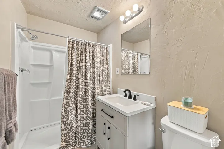 Primary Suite Bathroom featuring a white vanity cabinet with a stone-top surface and matte black hardware, integrated molded sink, matching matte black widespread faucet, and a white  shower surround