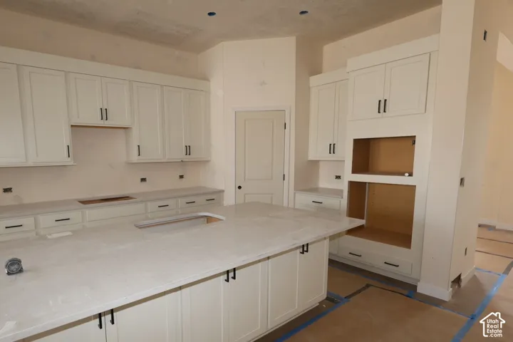 Kitchen featuring white shaker-style cabinetry, a large central island, solid-surface countertops, and built-in appliance enclosures