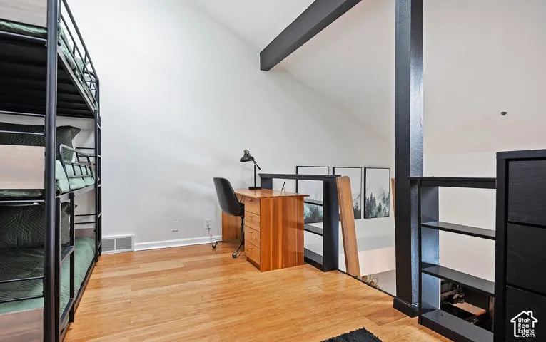 Open loft space featuring vaulted ceilings, wood-finish flooring, exposed support beams, and a railing with dark metal accents