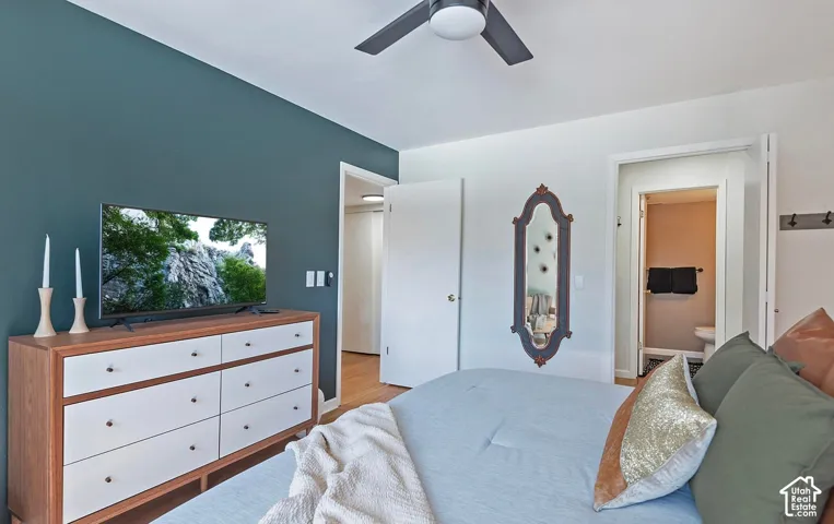 Room featuring a dark-toned accent wall, wood-finish flooring, and a ceiling-mounted fan with integrated lighting