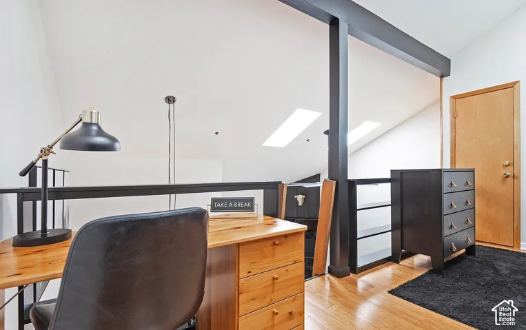 Vaulted ceiling with dual skylights, wood-finish flooring, and black metal structural support beams