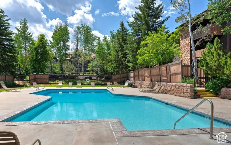 Outdoor swimming pool featuring a concrete deck, stone retaining wall, metal handrail, and perimeter wood fencing