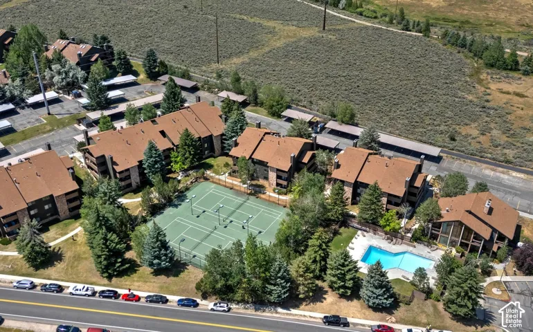 Aerial perspective of the residential complex featuring multi-story structures with pitched roofs, an on-site tennis court, and an outdoor swimming pool surrounded by mature trees