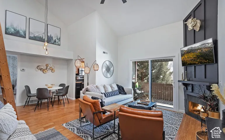 Vaulted ceilings, wood-finish flooring, floor-to-ceiling dark-toned fireplace surround, and sliding glass doors with balcony access