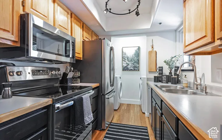 Kitchen featuring wood cabinetry, stainless steel appliances, solid-surface countertops, dual-basin stainless steel sink, and wood-finish flooring