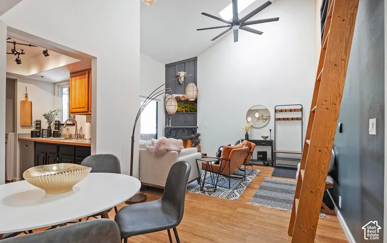 Vaulted ceilings featuring a multi-blade ceiling fan and skylight, wood-finish flooring, full-height decorative wall paneling, and an attached wood ladder