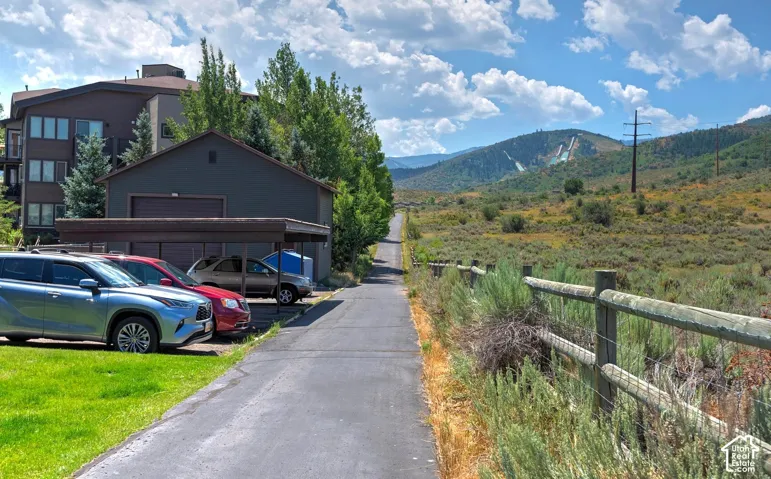 Asphalt access lane featuring a covered carport, detached structure, and mountain backdrop