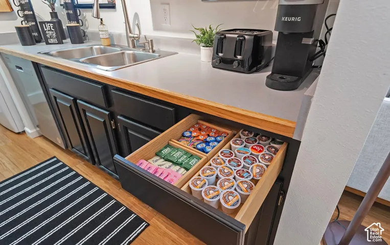 Counter area featuring dark cabinetry, a dual-basin stainless steel sink with a high-arc faucet, solid surface countertop, and a built-in drawer with integrated wooden dividers