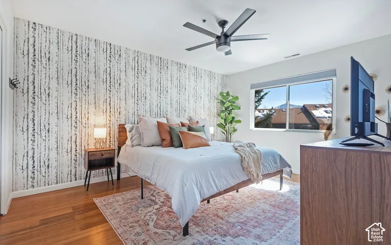 Room featuring wood-finish flooring, a matte black ceiling fan, and a patterned accent wall