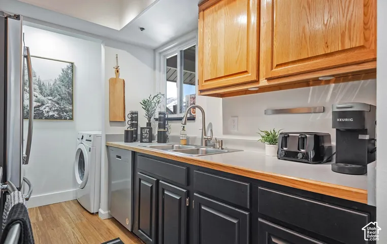Kitchen featuring two-tone cabinetry with wood-finish upper cupboards, contrasting dark lower cabinets, solid-surface countertops, stainless steel dual-basin sink with arched faucet, and wood-finish flooring
