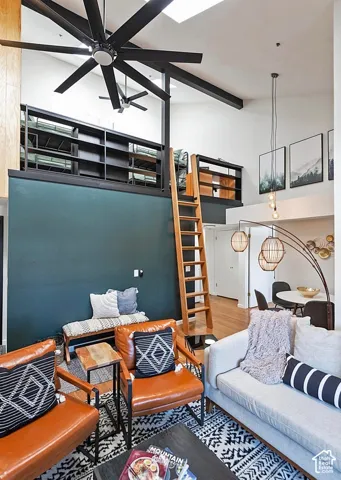 Vaulted ceilings featuring exposed structural beams, a multi-level loft area with integrated shelving, a wood-finish ladder, oversized industrial-style ceiling fan, and skylights