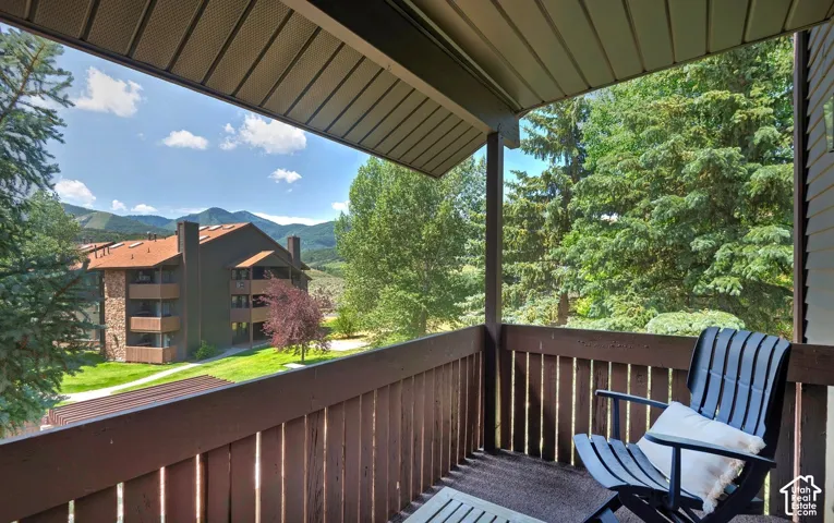 Covered balcony featuring a wood-slat railing and tongue-and-groove ceiling, overlooking mature pine trees and mountain terrain