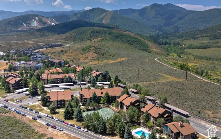 Aerial perspective featuring multi-story residential buildings, paved parking areas, a tennis court, a swimming pool, and a mountain backdrop
