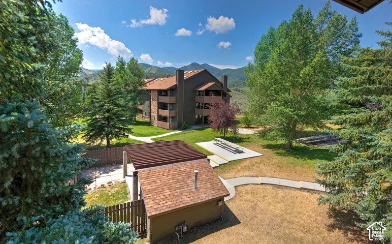 Exterior grounds featuring a multi-story building with stone-accented siding, a pergola-covered patio, paved walkways, mature evergreen trees, and a mountain backdrop