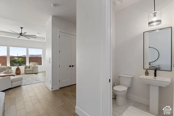 Powder room featuring a pedestal sink, framed mirror, and geometric floor tile, with wood-finish flooring, white panel doors, and a multi-blade ceiling fan in the surrounding space