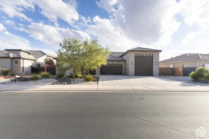 Stucco and stone facade featuring a three-car garage, concrete driveway, and xeriscaped front yard