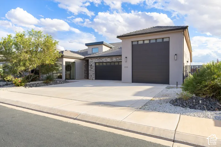 Modern exterior featuring stone veneer accents, multi-paneled garage doors, concrete driveway, and xeriscaped front grounds