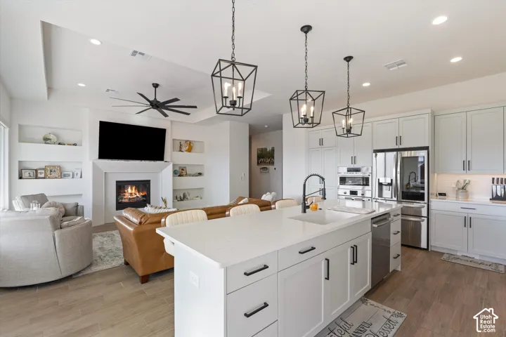 Open-concept interior featuring wood-finish flooring, a kitchen island with stone countertops, matte black geometric pendant lighting, built-in shelving flanking a fireplace, and ceiling fan