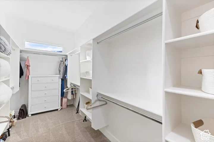 Walk-in closet featuring extensive built-in shelving, dual-level metal hanging rods, neutral carpeting, and an operable transom window