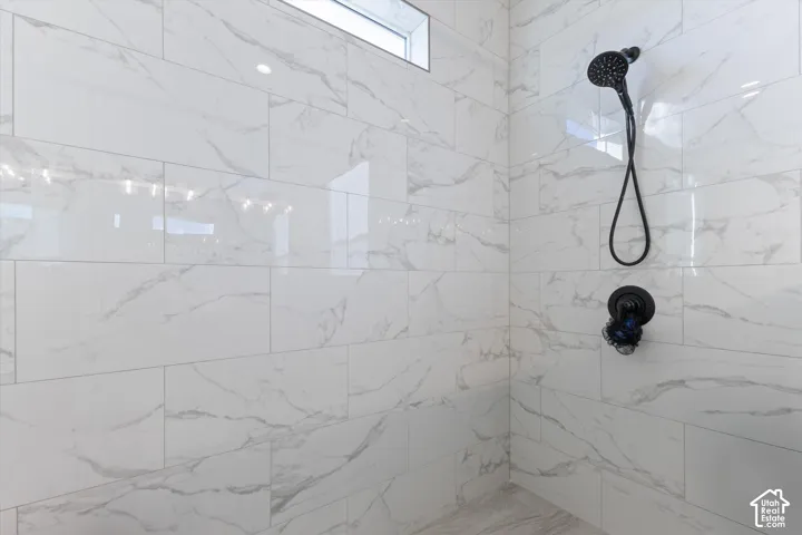 Shower enclosure featuring large-format white stone-finish wall tile with grey veining, a matte black rainfall shower head with handheld attachment, a coordinating matte black pressure balance valve, and a rectangular transom window