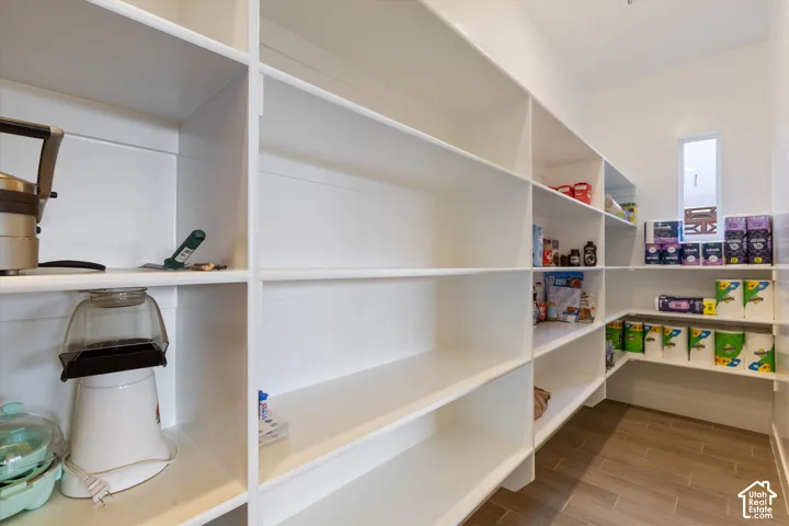 Walk-in storage space featuring floor-to-ceiling white built-in shelving, wood-finish tile flooring, and a vertical window