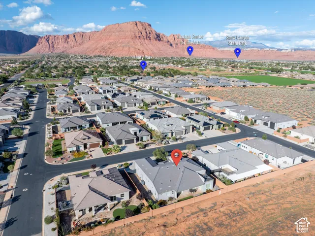 Aerial perspective featuring a residential property with a multi-pitch roof, integrated solar panels, and a fenced rear yard set against a mountain backdrop