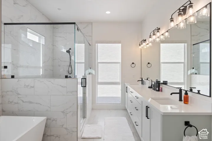 Bathroom featuring a dual-sink vanity with light-toned cabinetry, quartz countertops, a walk-in shower with floor-to-ceiling tile surround and matte black fixtures, and a soaking tub