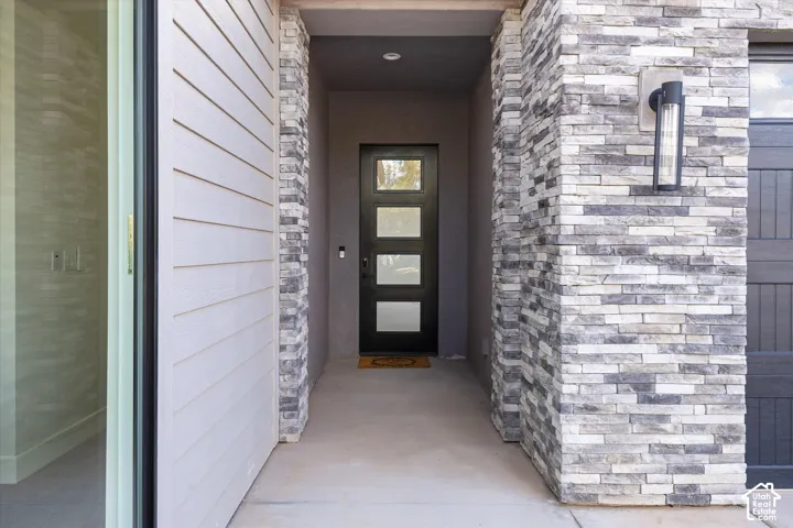 Entryway featuring stacked stone veneer siding, horizontal lap siding, modern rectangular door with glass panels, and matte black wall-mounted exterior lighting