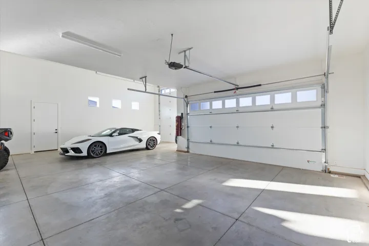 Spacious multi-car garage featuring a segmented sectional door with glass inserts, smooth concrete flooring, high ceilings, and inset accent windows