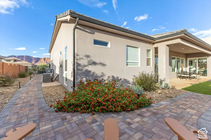 Stucco exterior featuring a covered patio, paved walkway, xeriscaped landscaping, and mountain backdrop
