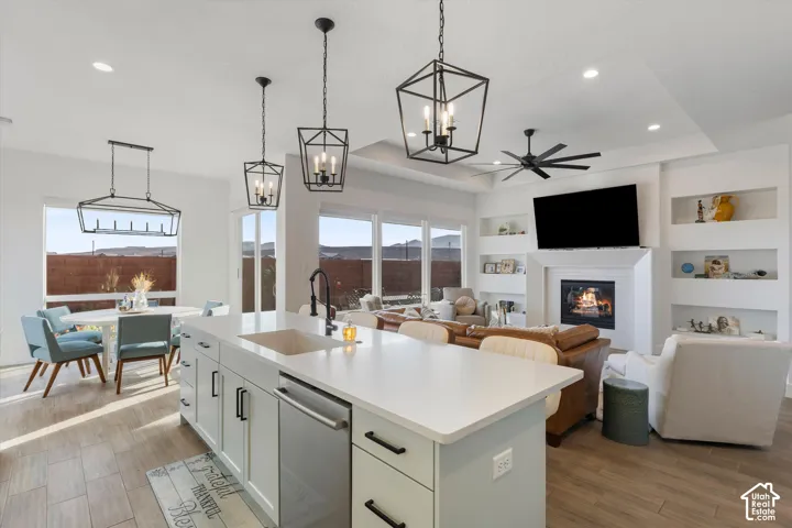 Kitchen island with stone-finish countertop, undermount sink, and matte black fixtures, complemented by tray ceilings, recessed lighting, geometric pendant lights, and a fireplace with integrated shelving