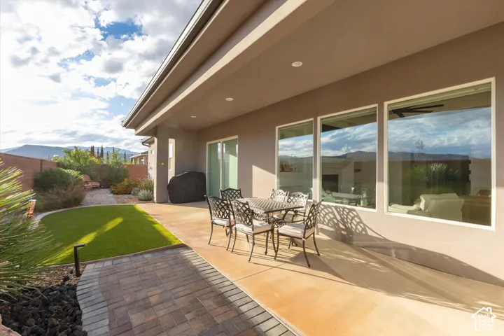 Covered concrete patio featuring recessed lighting, large picture windows, low-maintenance turf lawn, and decorative paver hardscaping