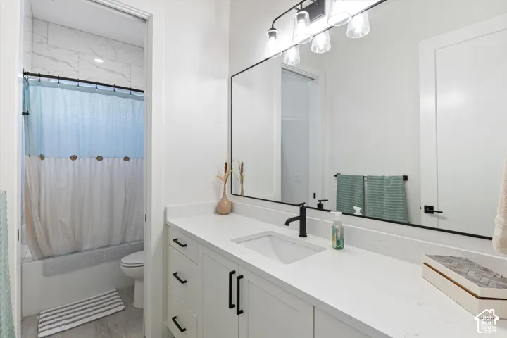Bathroom featuring a white vanity with stone-style countertop, undermount sink, matte black hardware, a full-width mirror with integrated lighting, and a bathtub with tile surround